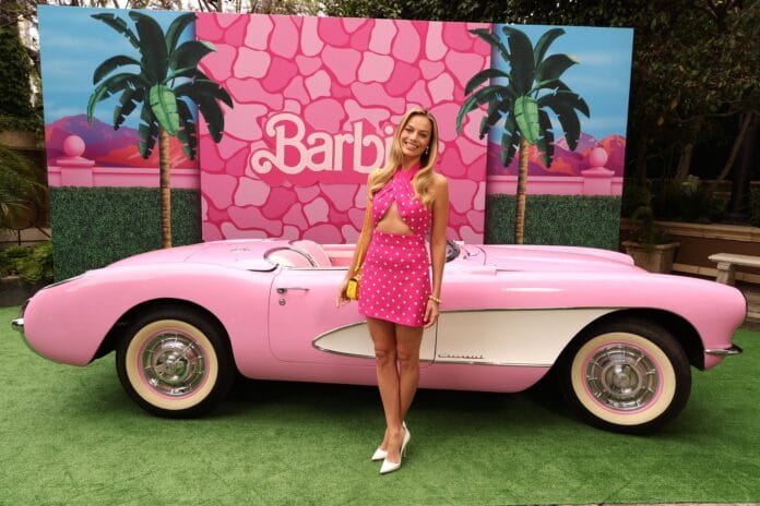 Margot Robbie Barbie-elokuvassa esiintyneen vaaleanpunaisen auton edessä.